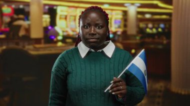 Kumarhane ortamında salvador bayrağı taşıyan kadının etrafı kültürel çeşitliliği yansıtan canlı kumar makineleriyle çevrili.