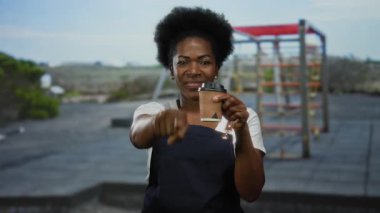 Elinde kahve fincanı tutan, önlük giymiş arka planda parmak atletik ayarı gösteren bir kadın..