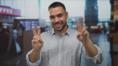 Kalabalık havaalanı terminalinde barış işareti yaparken gülümseyen adam, gençlik iyimserliği..