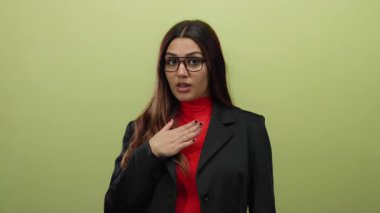 Kırmızı bluzlu ve siyah ceketli bir kadın izole edilmiş sarı arka planda duruyor. Şaşırmış ve düşünceli görünüyor..