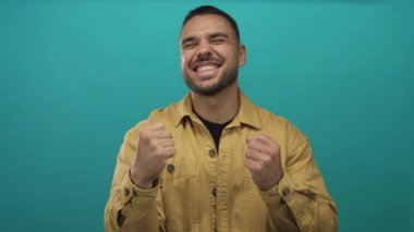 Hardal gömlekli adam stüdyo ortamında seramik zemine sahip yumruklarını ve suratını sıkar; hüsran dürtüsü azmi.