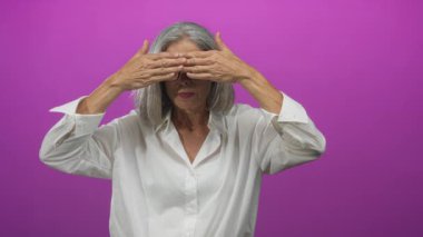 Gri saçlı, gözlüklü bir kadın, elleri alnına kaldırıyor ve avuçları morumsu stüdyoda hareket ediyor. Sürpriz bir kutlama..