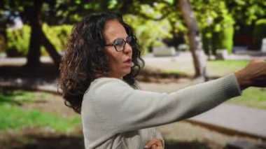 Kıvırcık saçlı bir kadın sanki canlı bir park ortamında halat çekiyor gibi neşeli ve anlamlı bir tavırla güneşli ağaçların altında neşeli bir anı yakalıyor..