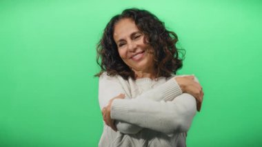 Gözleri kapalı gülümseyen bir kadın yeşil bir arka plana sarılıyor sıcaklığını ve memnuniyetini iletiyor..