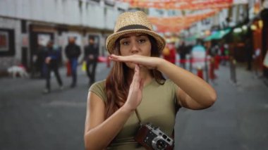 İşlek bir sokak sahnesinde şapka takan İspanyol kadın, boynunda kamera, bulanık yayalar ve canlı süslemelerle takılıyor.