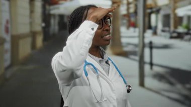 Steteskoplu beyaz önlüklü kadın doktor gözlüklü ve odaklanmış bir şekilde şehir sokaklarında arama yapıyor..