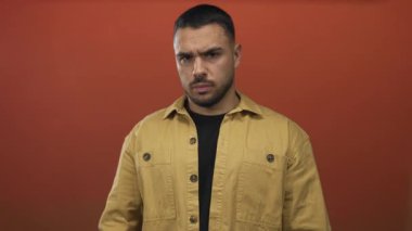 Sarı ceketli bir adam stüdyoda sessizlik için kaşlarını çatıyor ve parmaklarını dudaklarına sürtüyor..