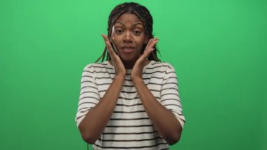 Elleri yanaklarına bastırılmış, geniş gözlü, ağzı açık yeşil perde stüdyosunda çizgili gömlek ve örgü takan bir kadın..