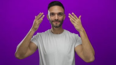 İspanyol asıllı bir adam coşkuyu ifade ediyor, elleri havada, mor arka planda, rahat beyaz bir gömlek giyiyor, heyecan ve sürpriz taşıyor..