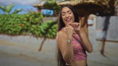 Kol saatini gösteren renkli bir tişört giyen genç İspanyol kadın evin duvarının yakınındaki girişe başparmak işareti yapıyor..