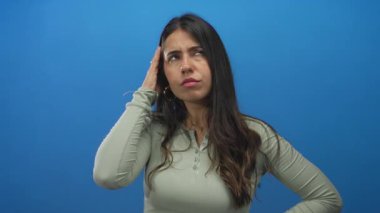 İzole edilmiş mavi duvarın üzerinde kafa yoran genç bir İspanyol kadın. Düşünceli duygularını ifade ediyor. Elleri çenesinde, günlük kıyafetleriyle..