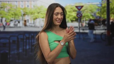 Meşgul bir şehir caddesinde el çırpan bir kadın yeşil kırbaç üstü ve kol saati içinde, gülümseyen ve hareket eden;.