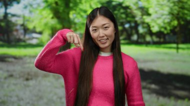 Güneşli bir günde, arka planda mutlu ve huzurlu görünen ağaçlarla dolu yemyeşil bir parkta pembe süveter giyen kadın..