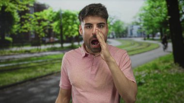 Yeşil parkta yapraklı ağaçların ve asfalt yolların altında bağırırken pembe gömlekli bir adam kıt kanaat geçiniyor..