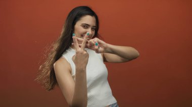 Canlı turuncu arkaplan ile bir fotoğraf stüdyosunda hashtag jesti oluşturan gülümseyen İspanyol kadın, popüler oyunculuk.