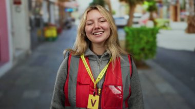Şehir sokaklarında gülümseyen kırmızı gönüllü yelek giyen bir kadın şehir manzarası arasında neşe ve bağlılığını gösteriyor..