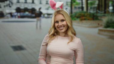 Tavşan kulaklı bir kadın, şehir ortamında neşeli bir an yakalıyor, gün boyunca bulanık binalar ve yayalarla çevrili..