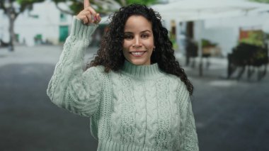 Genç İspanyol kadın, gündüz vakti şehir sokaklarında dikilirken heyecanla gülümsüyor ve işaret ediyor.