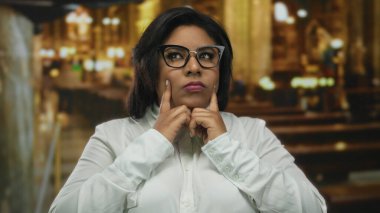 Kilisede el ele tutuşan, düşünceli düşüncelere dalan, gözlük takan, samimi bir anda yakalanan, kültür ve kimliğe önem veren bir kadın..