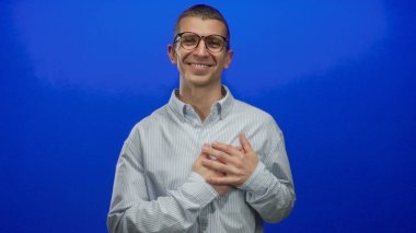 Çizgili tişörtlü, gülümseyen beyaz adam, göğsünde elleriyle, izole ve sakin bir arka plana karşı şükranlarını sunuyor..