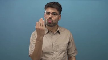 Mavi stüdyoda gözlüklü, büzüşmüş dudaklı ve çimdiklenmiş parmaklı İspanyol bir adam jest yapıyor..