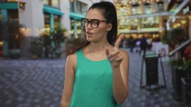 Meşgul bir sokak alışveriş bölgesinde gözlük ve yeşil kolsuz bluz giyen genç bir İspanyol kadın işaret parmağı sallıyor..