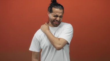 Portakal rengi duvarlı bir stüdyoda beyaz bir tişört giyerken omzunu sımsıkı tutan ve irkilen İspanyol genç bir Arap..