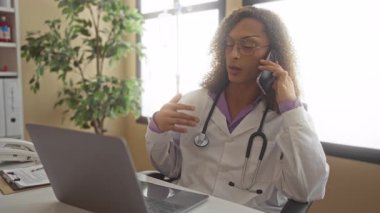 Steteskop kullanan transseksüel kadın doktor telefonu kulağına tutuyor ve klinikte elle klavyeyi dinliyor;.