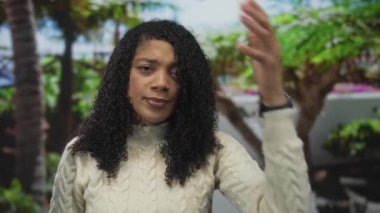 Beyaz kazaklı kadın, ormanda yemyeşil yaprakların arasında, tarafsız bir ifadeyle el ele tutuşuyor..