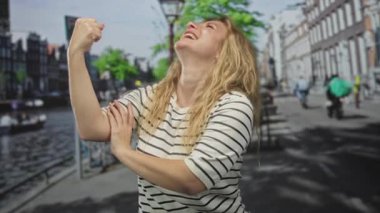 Kadın gülümserken kollarını esnetir ve kanalın kenarına doğru pazılarını bastırır..