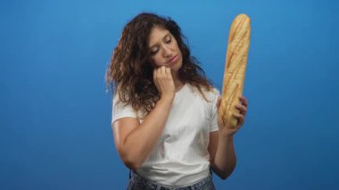 Baget tutan kadın, el yanak ve mavi stüdyo aşağı bakıyor, beyaz tişört ve kıvırcık saçlı kot pantolon giyiyor; tefekkür.