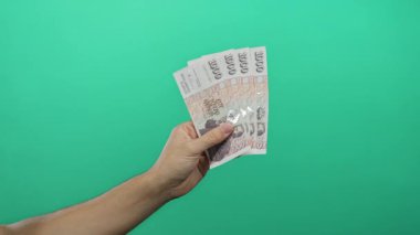 Yeşil arka planda İzlanda Krona banknotları tutan adam, tecrit edilmiş bir ortamda mali başarı ve para birimi kavramlarını gösteriyor.