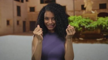 Genç İspanyol kadın, eski bir kasaba sokaklarına para harcamak için sakince parmak uçlarını ovalıyor; tüketim alışverişi alışveriş harcamaları perakende satış finansmanı ekonomi ödeme bütçesi.