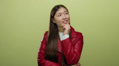 Kırmızı ceketli kadın, izole edilmiş sarı arka planda poz veriyor. Uzun saç ve delinmiş kulaklarla güçlendirilmiş düşünceli bir ifade çiziyor..