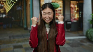 Canlı şehir caddesinde kendine güveni tam kırmızı ceketli bir kadın neşeli ifadesini gösteriyor.