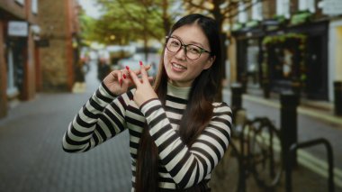 Açık havada gülümseyen bir kadın canlı bir şehir caddesinde hashtag jesti yapıyor. Gençlik enerjisini ve modern iletişimi somutlaştırıyor..