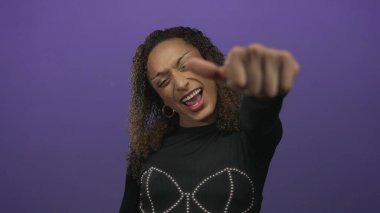 Gülümseyen ve baş parmak işareti yapan bir kadın canlı mor bir stüdyoda görünür bir el ile; sevinç kutlaması.