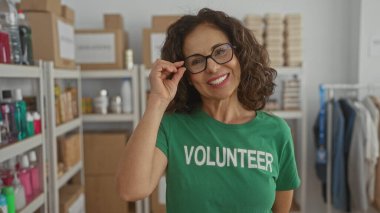 Yardım odasında gülümseyen bir kadın gönüllü gömleği giyiyor. Kapalı alanda gönüllü bir kadın. Organize raflarda yardım malzemeleri sergiliyor..