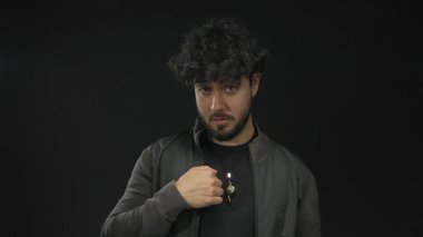 Sakallı ve kıvırcık saçlı genç adam siyah bir arkaplana karşı jest yapıyor, koyu renk ceketli ve gündelik kıyafetli oyuncu ve düşünceli bir tavır sergiliyor..