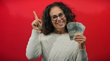 Endonezya rupia banknotları tutan ve canlı kırmızı bir arkaplana doğru bakan, mutluluk ve parasal başarı gösteren bir kadın..