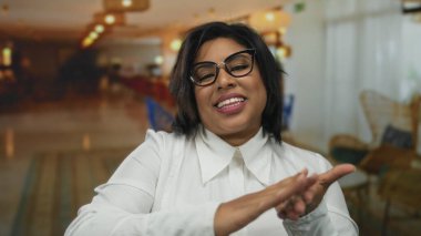 Kapalı bir otelde gülümseyen gözlüklü bir kadın rahat ortam ortamında para harcıyor ve finansal mizah gösteriyor..