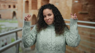 Roma harabelerinde şakacı hareketler yapan bir kadın eski mimari ile arka planda gelişigüzel giyinmiş genç bir İspanyol kadını sergiliyor..