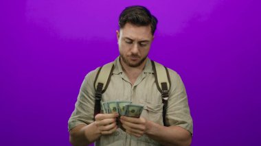 Sırt çantalı genç bir adam, canlı bir mor arka planda dolar sayıyor, bir gezgin ya da turist havasını somutlaştırıyor, finansal planlama ya da macera ima ediyor..