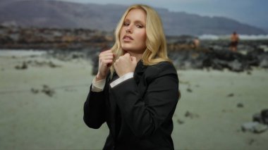 Kumsalda takım elbiseli bir kadın, güçlendirme konsepti için sahilin manzaralı arka planına karşı yumruklarıyla poz veriyor.