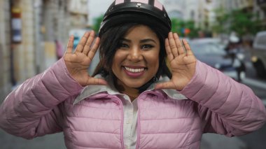 Kasklı ve pembe ceketli bir kadın şehir merkezinde pozitiflik ve açık hava macerası sergiliyor..