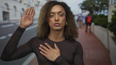 Kadın bej sokakta göğüs göğüse, halka küpeli, gözle görülür ve doğrudan bir bakışla; empati dayanışması içtenliği..