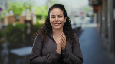 Terasta neşeli bir şekilde gülümseyen kadın, arka planda canlı bir sokak bulunan canlı, kentsel bir sahneyi yakalar, mutluluk ve rahatlamış bir ortam hissi taşır..