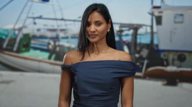 Deniz kıyısındaki limanda parmaklarıyla el kol hareketi yapan, donanma elbisesi giyen, arka planda tekneleri olan bir kadın, sahil şeridi boyunca gelişigüzel bir açık hava sahnesini yakalıyor..