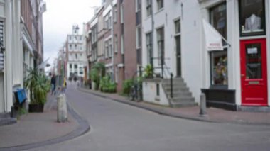 Bulutlu gökyüzünün altında kırmızı kapılı ve bisikletli bir Amsterdam caddesinin bulanık görüntüsü şehir cazibesini ve mimarisini sergiliyor..