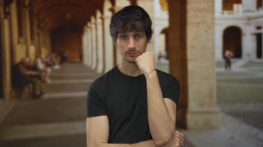 Üniversite binasında el pençe divan duran siyah tişörtlü genç adam; yalnızlık iç gözlem meditasyonu yansıması.